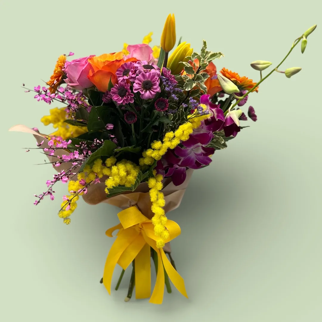 Mazzo grande di mimosa con rose, tulipani, gerbere e margherite nei toni arancio e fucsia, legato con un nastro giallo