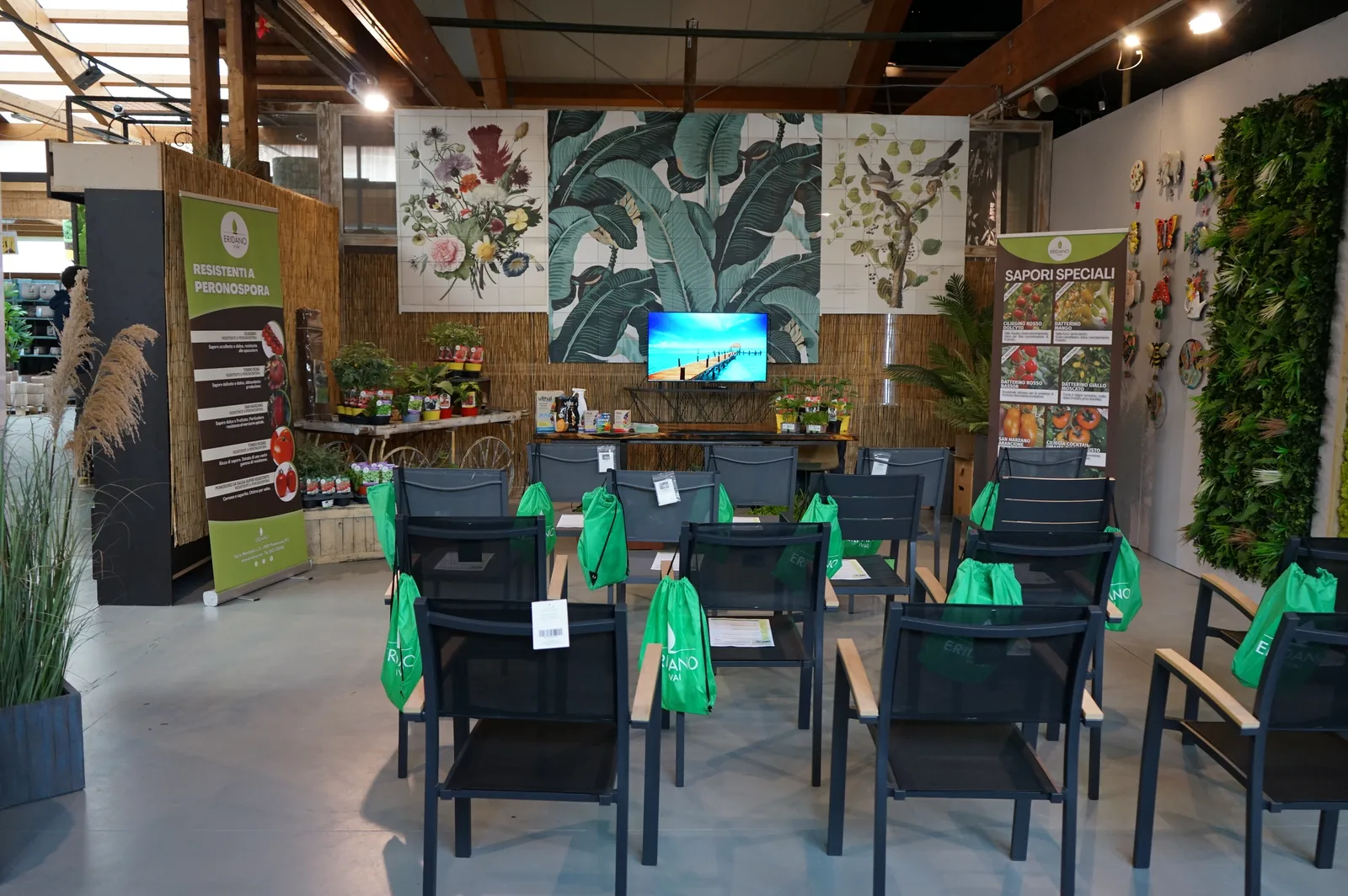 La sala della serra preparata per il corso, con file di sedie nere, una sacca verde su ogni sedia e gli espositori delle piantine in fondo