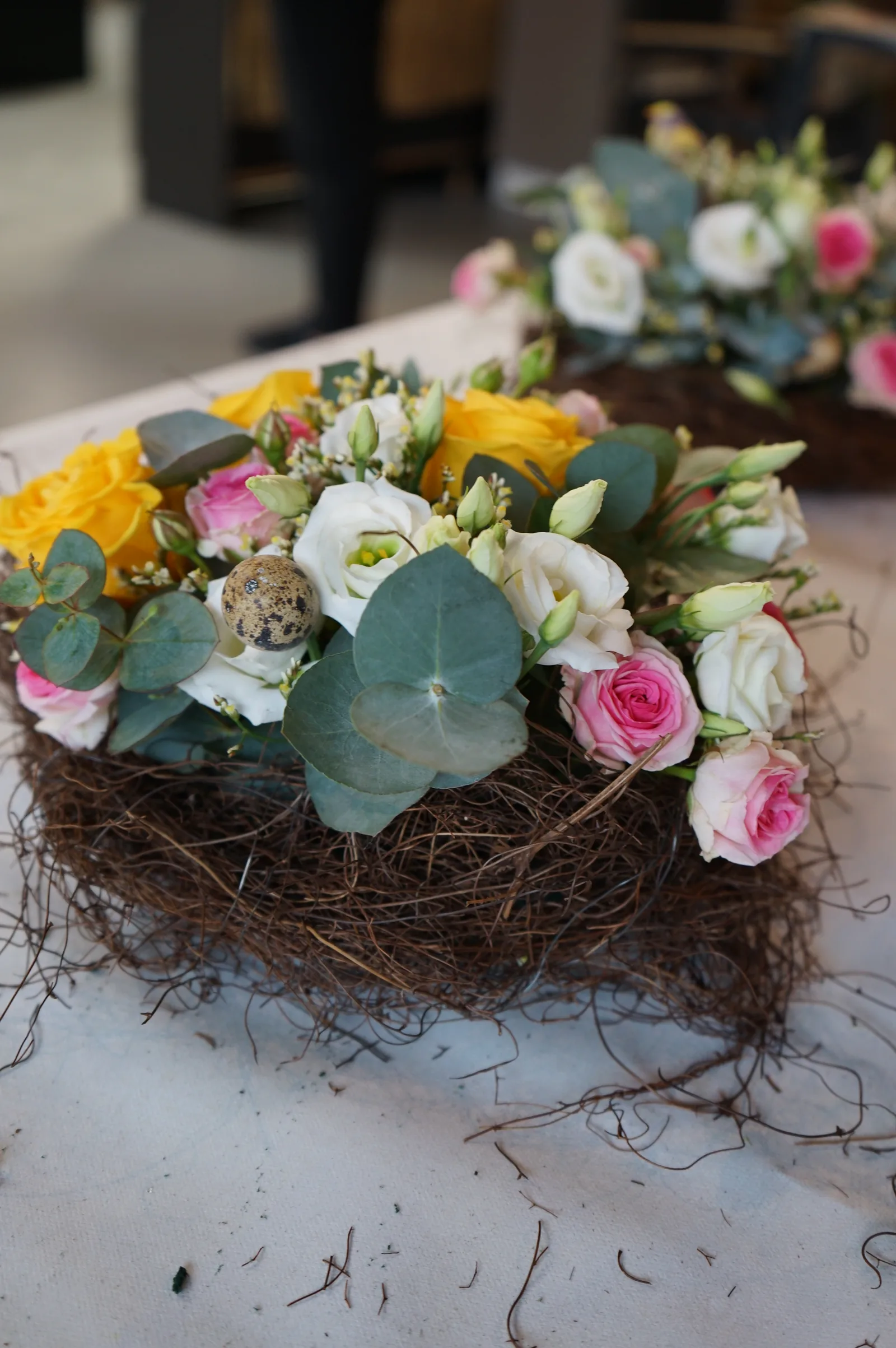 Nidi di rami con rose gialle, lisianthus rosa ed eucalipto allineati sul tavolo