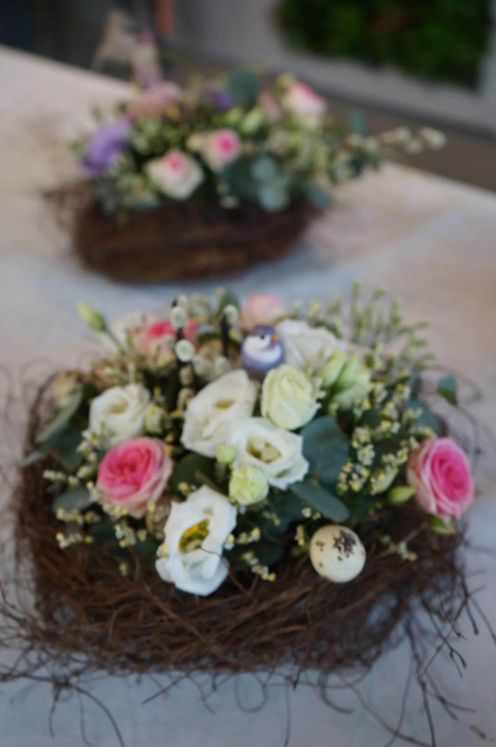Nido di rami con lisianthus bianchi e rose rosa, e un uccellino azzurro in mezzo ai fiori