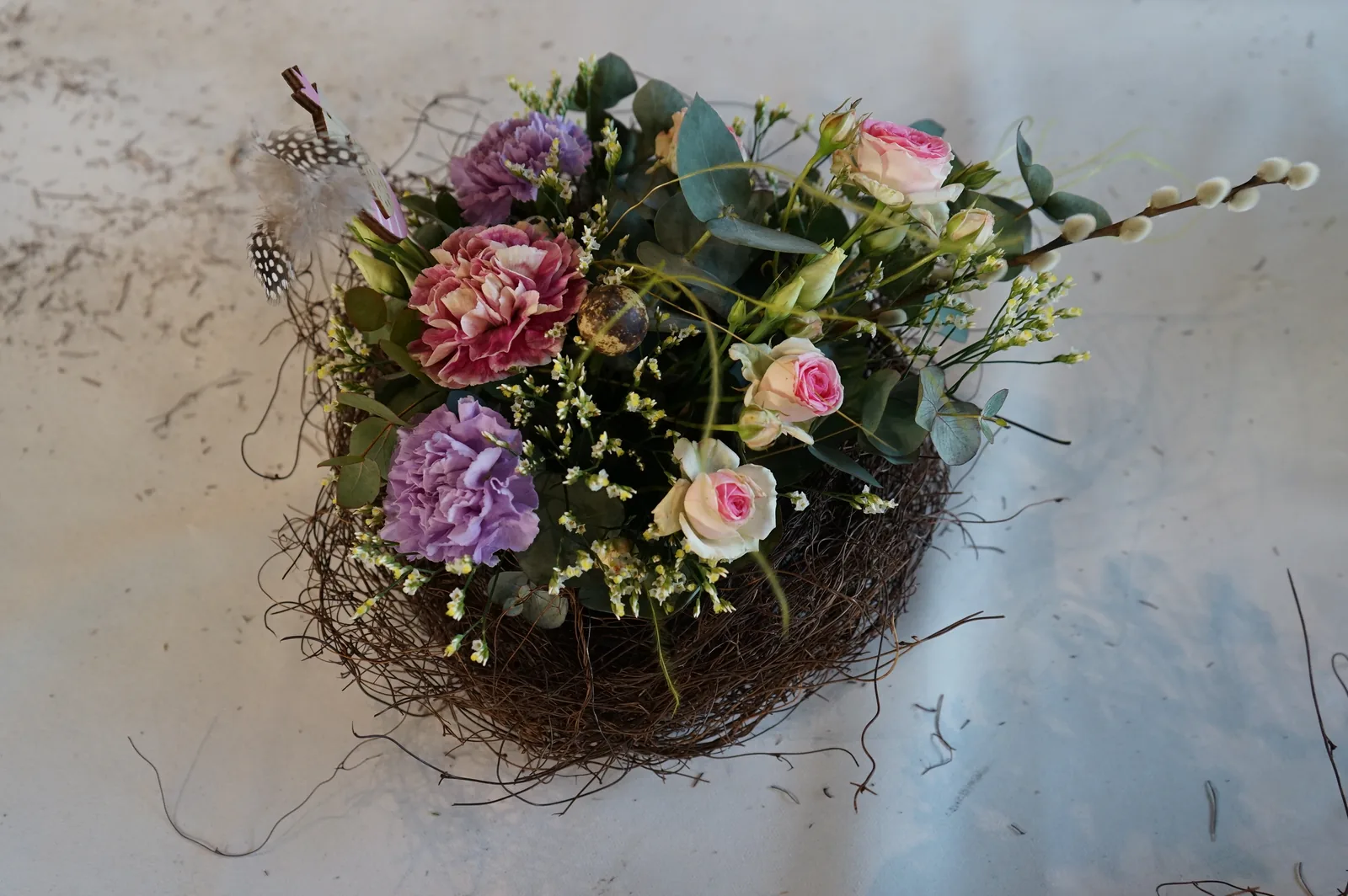 Un centrotavola nel nido di rami visto dall'alto, con garofani viola e rose rosa