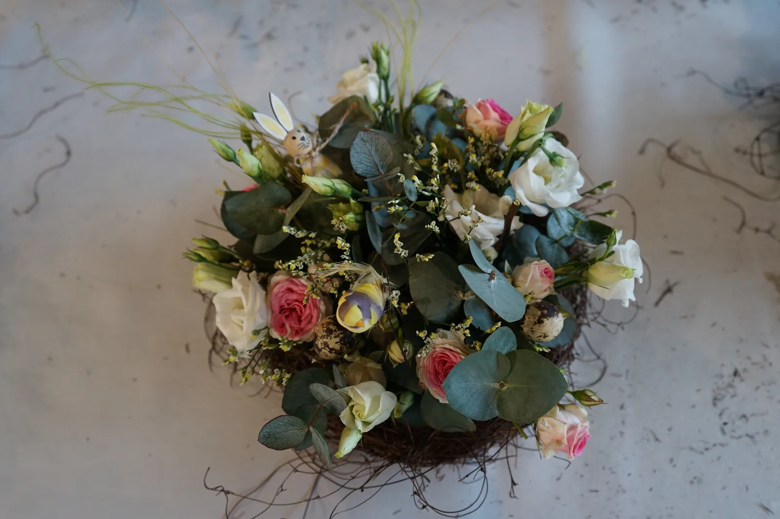 Un centrotavola di Pasqua visto dall'alto: un nido di rami con rose, lisianthus ed eucalipto sul tavolo