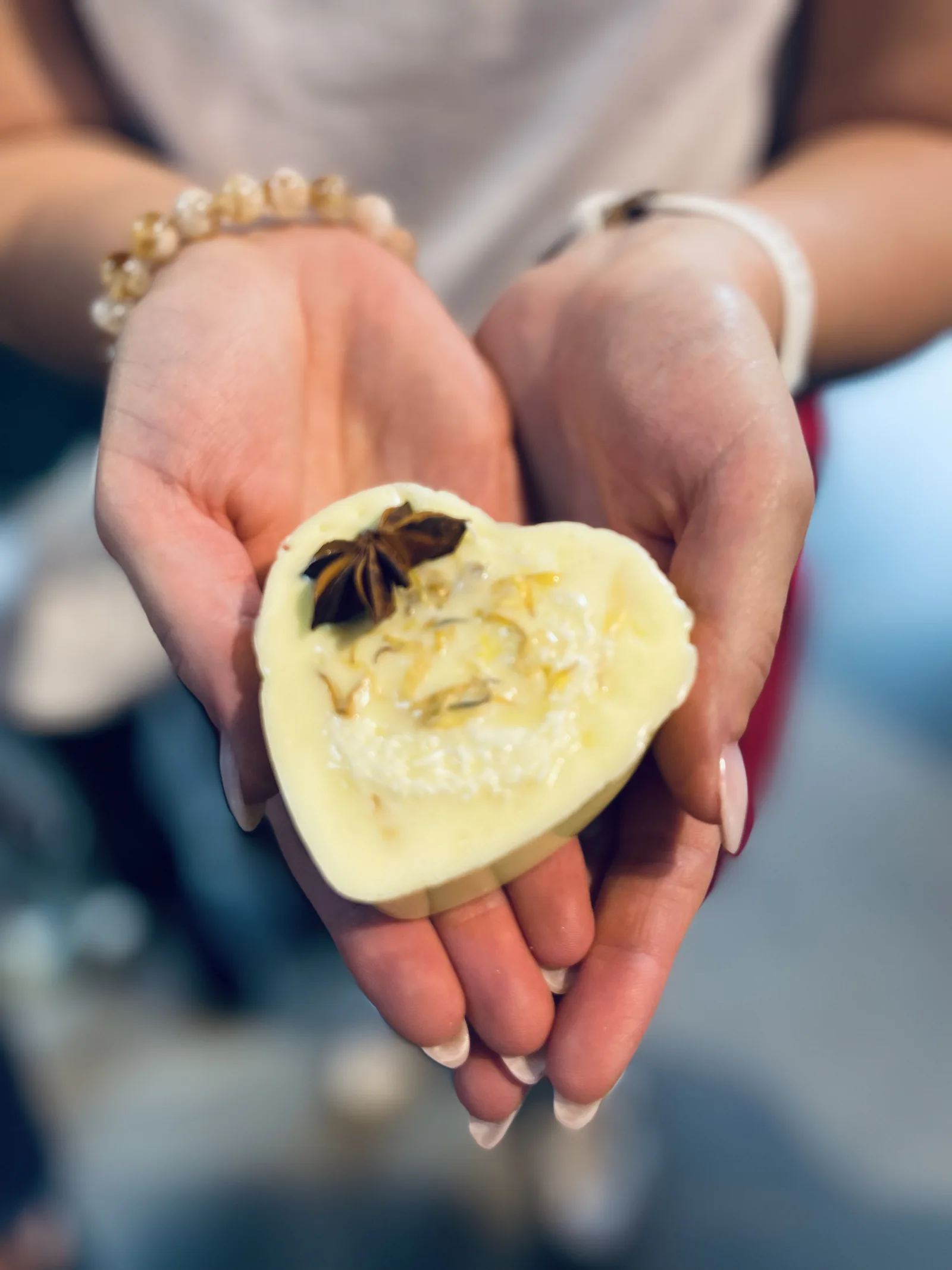 Un sapone color crema a forma di cuore con l'anice stellato, fra due mani