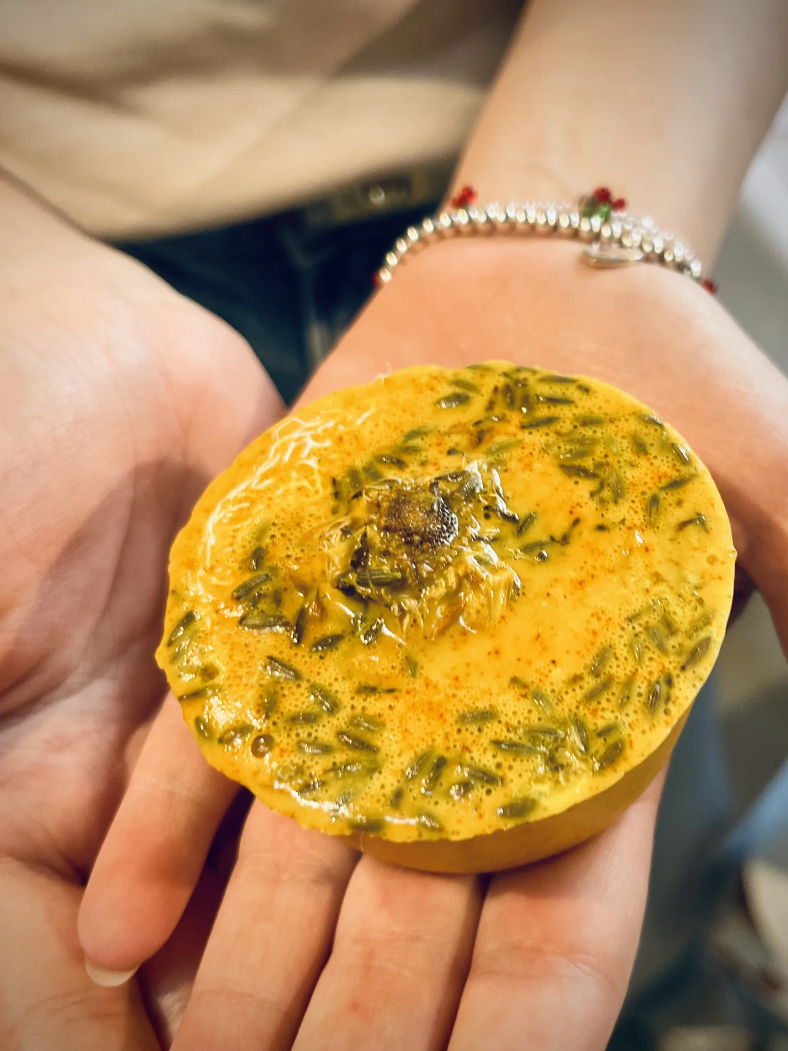 Un sapone giallo rotondo con le erbe secche, sul palmo di una mano