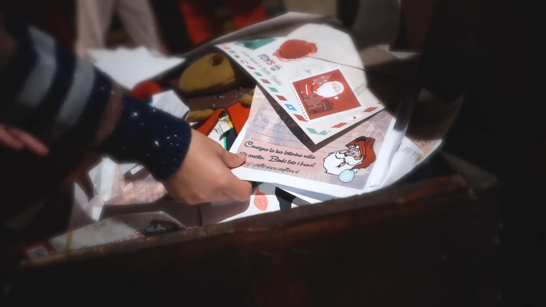 Una mano infila una letterina per Babbo Natale in una cassetta di legno piena di lettere