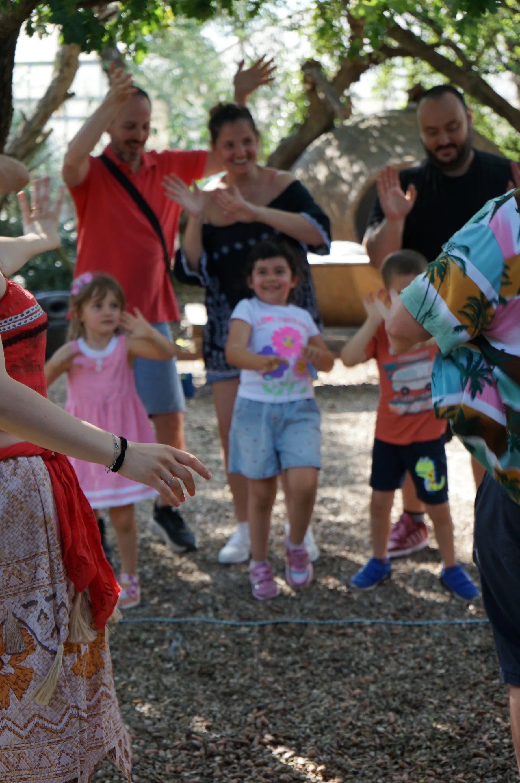 Bambini che ballano sulla ghiaia a braccia alzate, con i genitori dietro che battono le mani e il vestito di Vaiana in primo piano