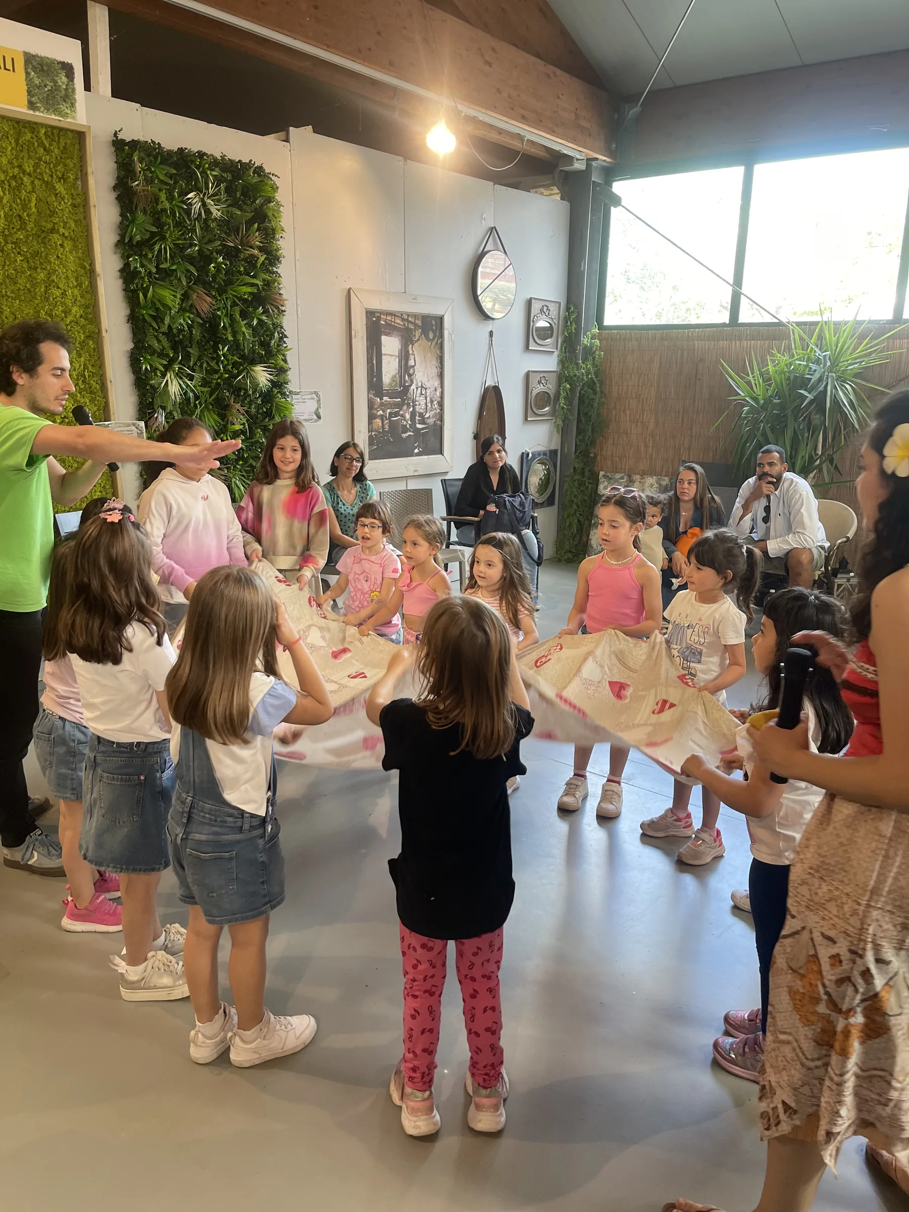 Bambini in piedi in cerchio reggono i bordi di un grande telo chiaro, con un animatore che indica e Vaiana di spalle
