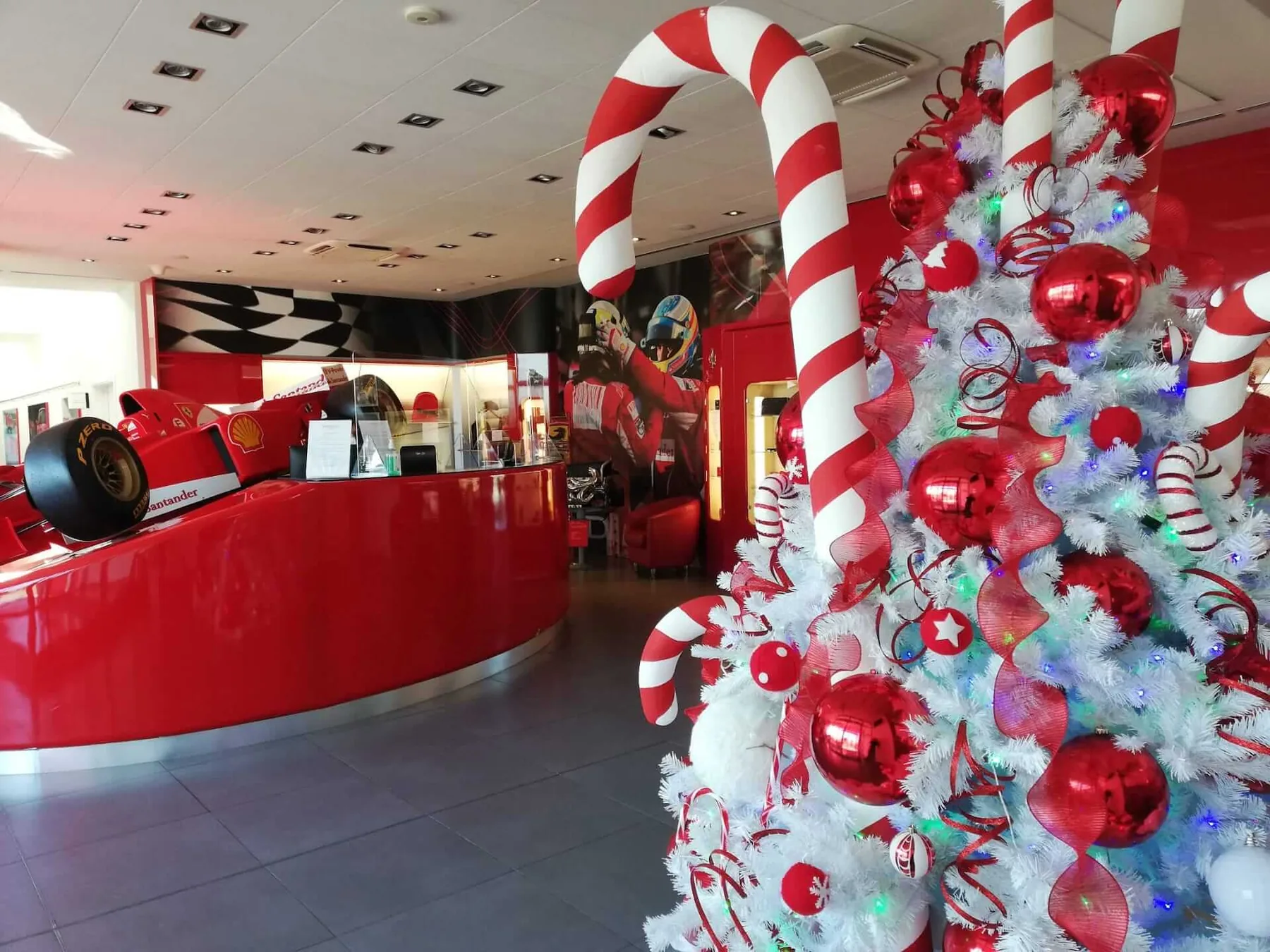 Albero bianco con palline rosse e bastoni di zucchero giganti nell'ingresso di uno showroom con un'auto da corsa rossa