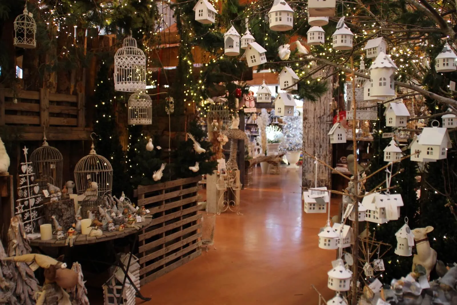 Corridoio di alberi addobbati con casette bianche appese, gabbiette e pallet di legno