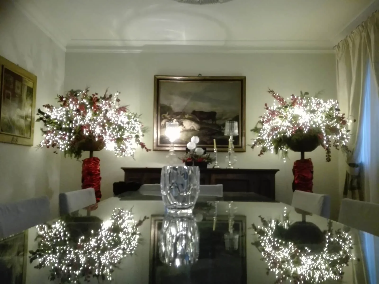 Sala da pranzo con tavolo di cristallo e due composizioni di fiori illuminati su vasi rossi