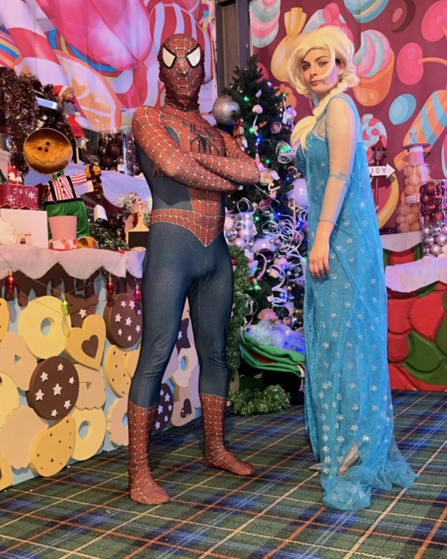 Spiderman ed Elsa di Frozen in posa davanti a un fondale di dolci colorati e a un albero di Natale