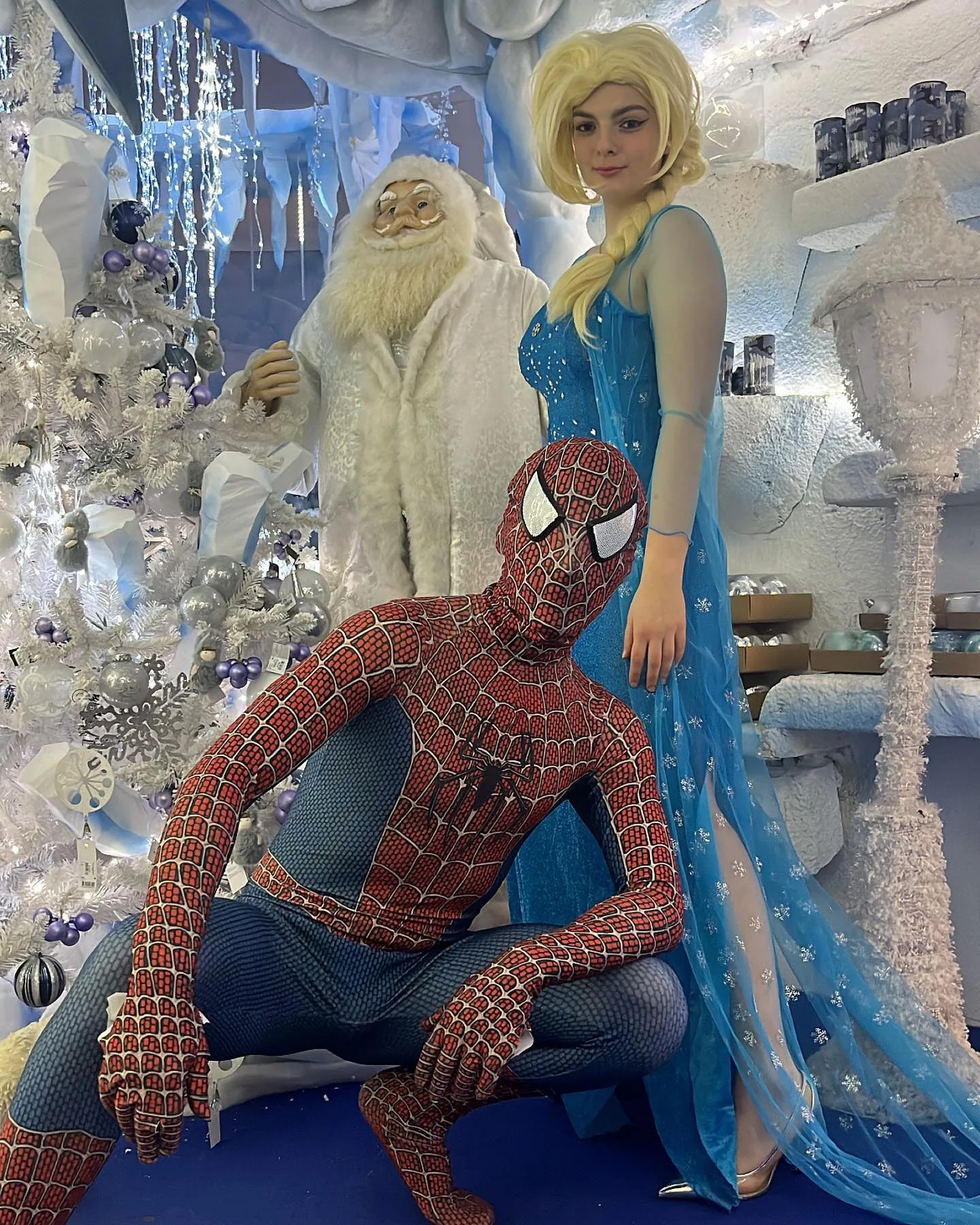 Spiderman accovacciato ed Elsa in piedi accanto a un Babbo Natale bianco, fra alberi innevati