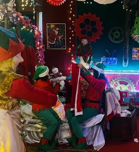 Elfi e Babbo Natale nella camera rossa e verde, fra ingranaggi decorativi e festoni