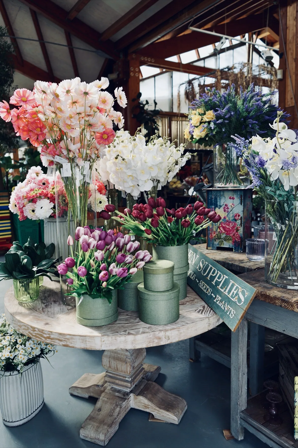 Tavolo rotondo con fiori artificiali: cosmee rosa, orchidee bianche, tulipani viola e bordeaux