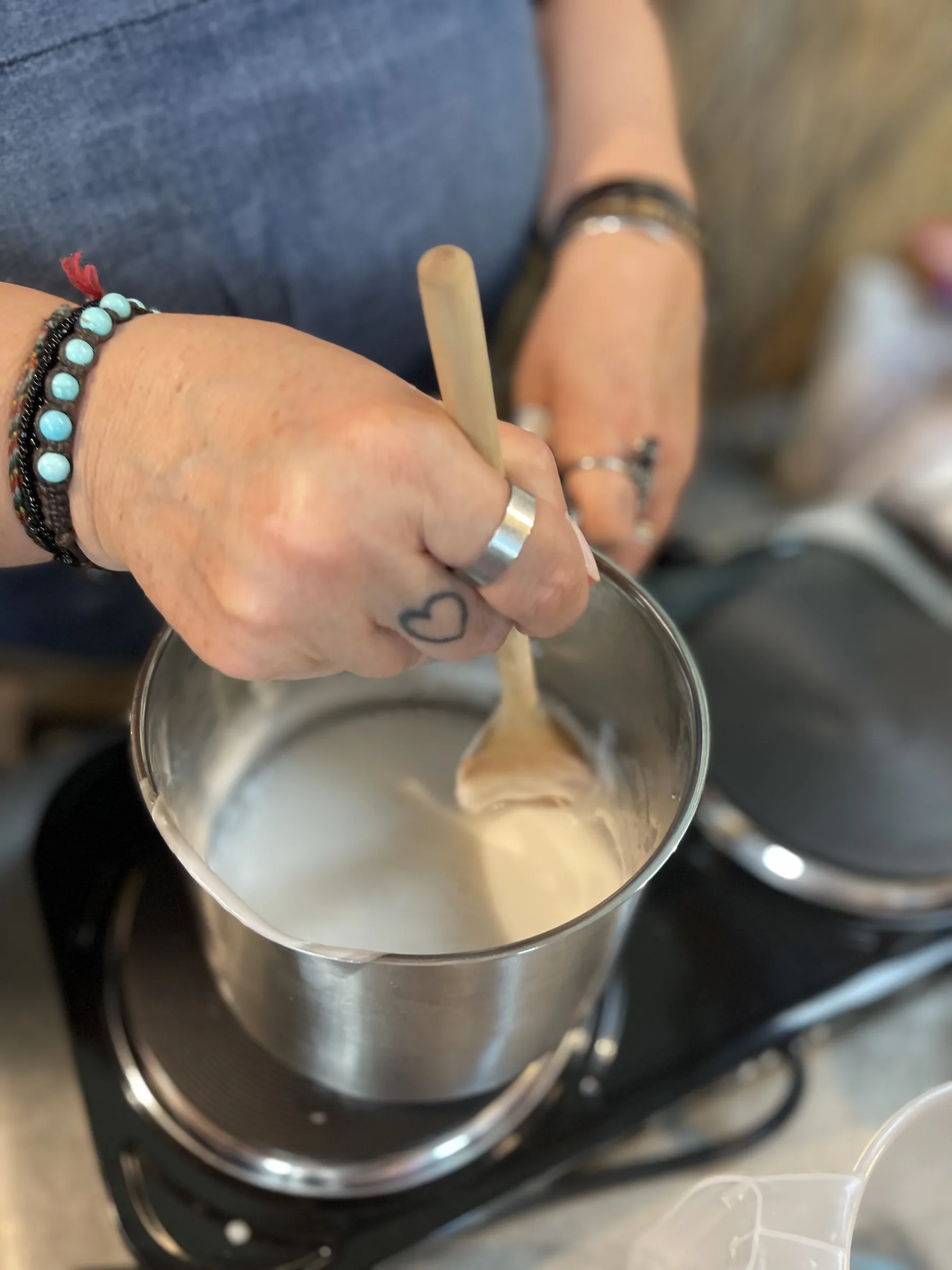 Una mano mescola il sapone fuso in un pentolino sul fornello