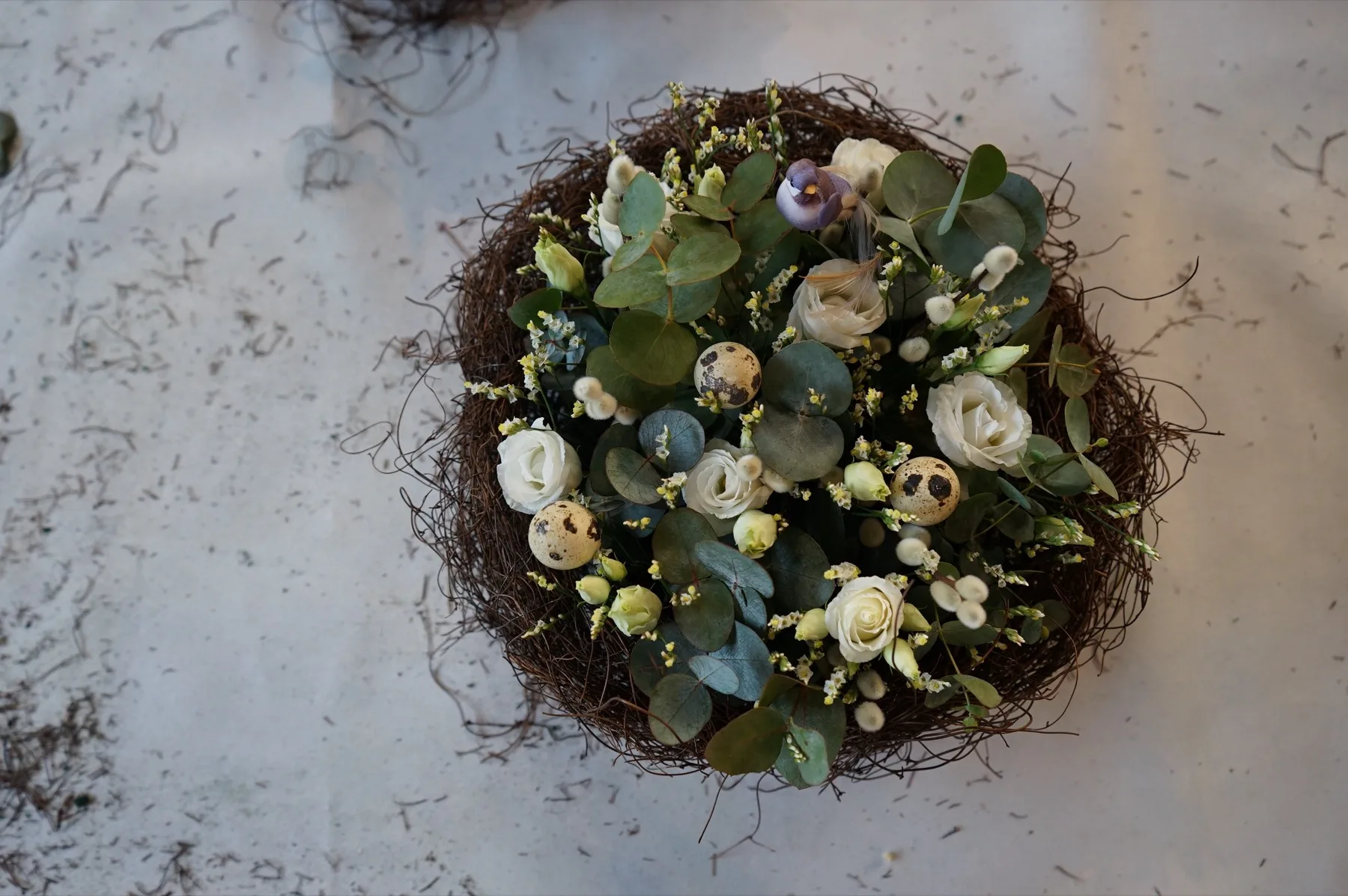 Composizione vista dall'alto: lisianthus bianchi, eucalipto e uova di quaglia dentro un nido di rami