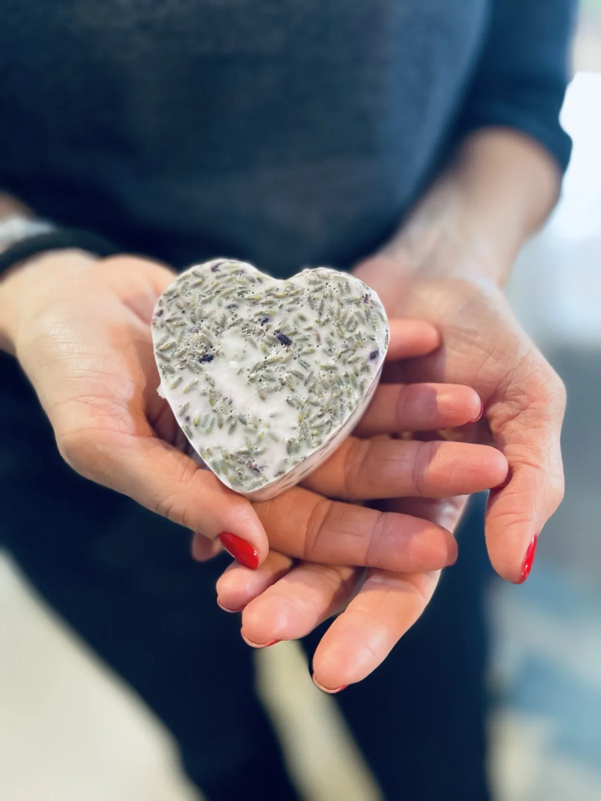 Due mani tengono un sapone a forma di cuore con fiori di lavanda in superficie