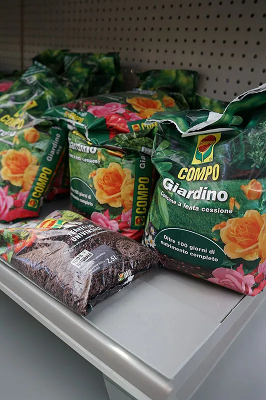 Sacchi di terriccio per giardino con i fiori stampati, appoggiati sul bancale del reparto insieme a un sacco aperto