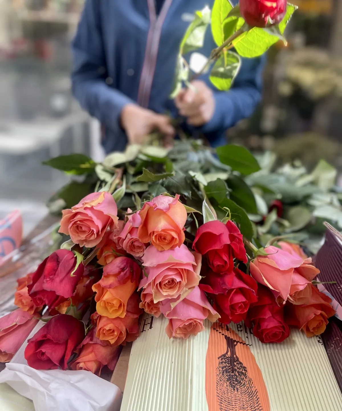 Rose rosse e arancioni distese sulla carta da incarto, sul piano del banco, mentre due mani ne tengono una per il gambo