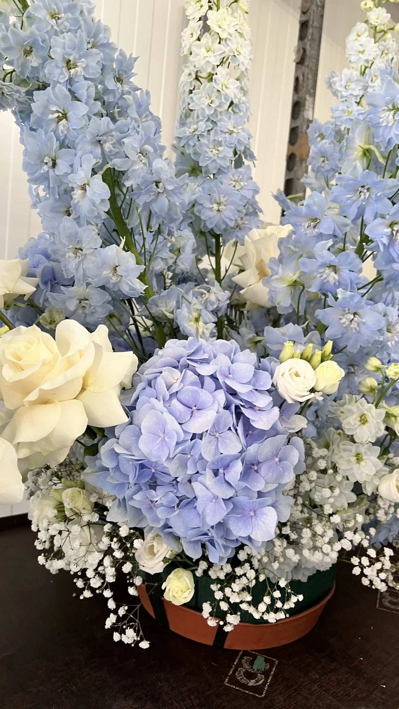 Grande composizione di ortensie e delphinium azzurri, rose bianche e gypsophila in un vaso basso