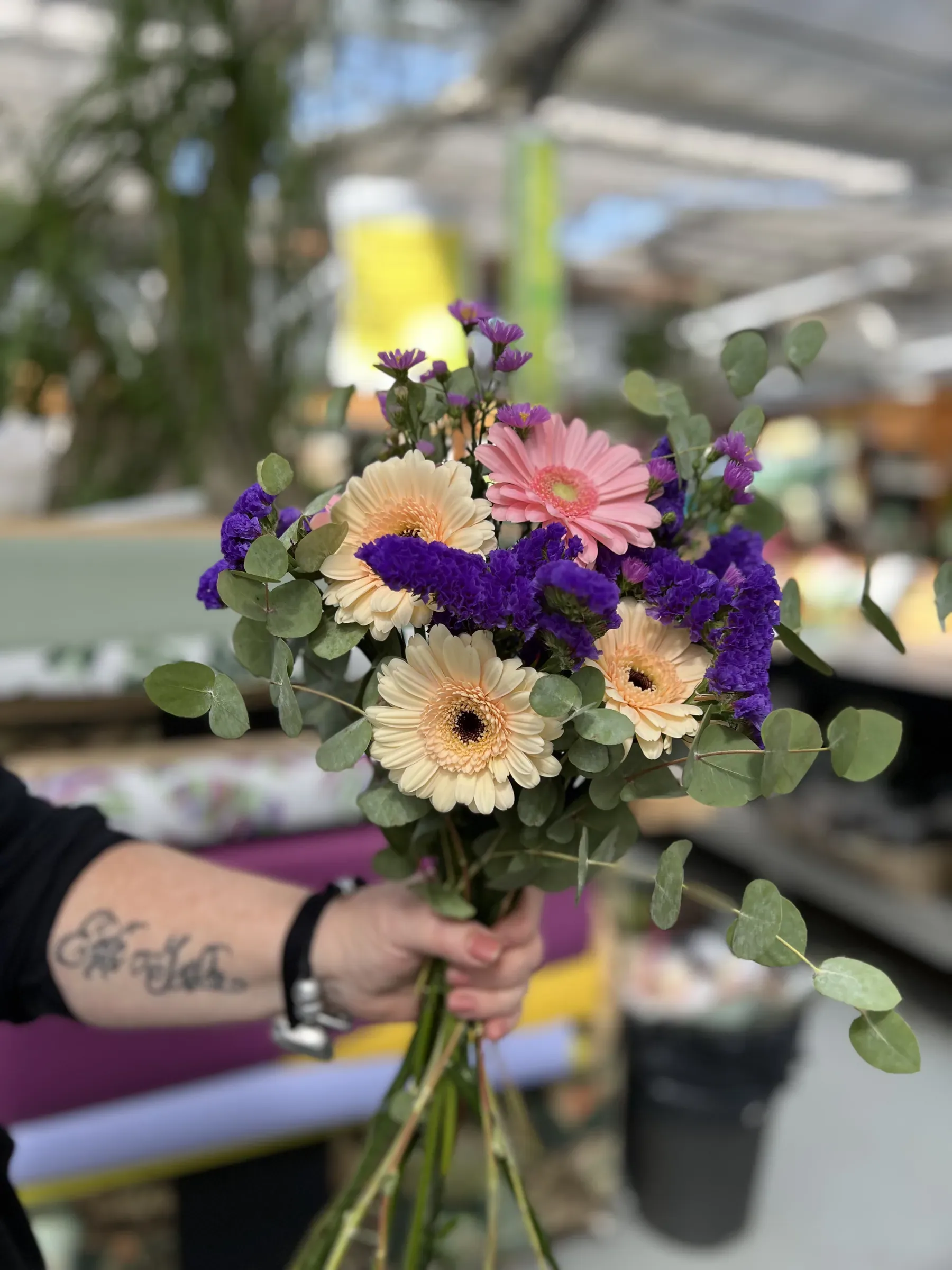 Mazzolino di gerbere color crema e rosa con fiori viola ed eucalipto, legato a mano e tenuto per i gambi