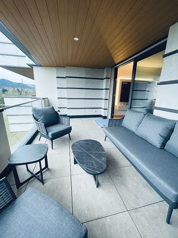 Loggia con divano e poltroncine da esterno grigie sul pavimento chiaro, sotto il soffitto in legno