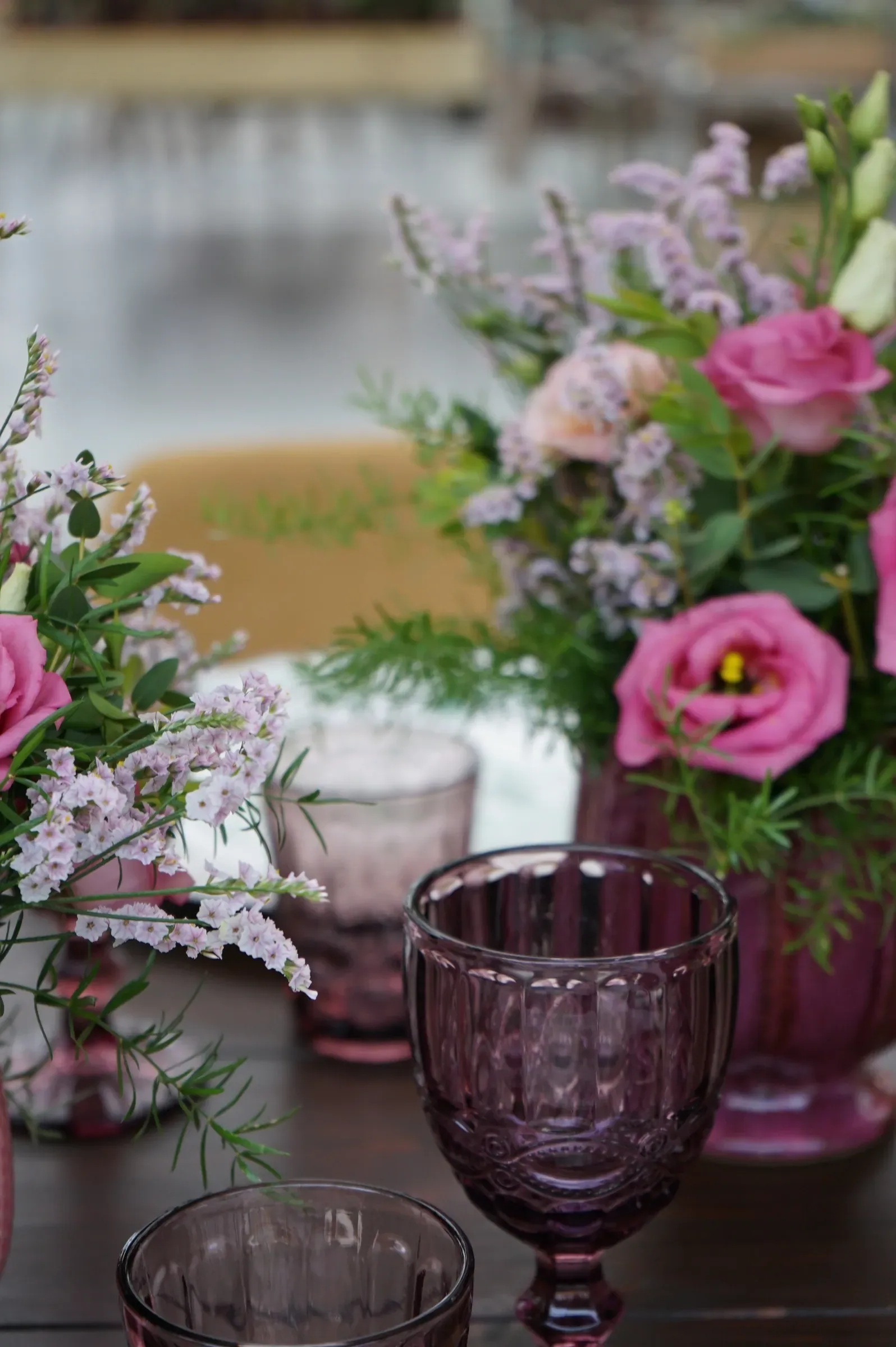Lisianthus rosa e fiori lilla nei vasi, dietro un calice di vetro viola