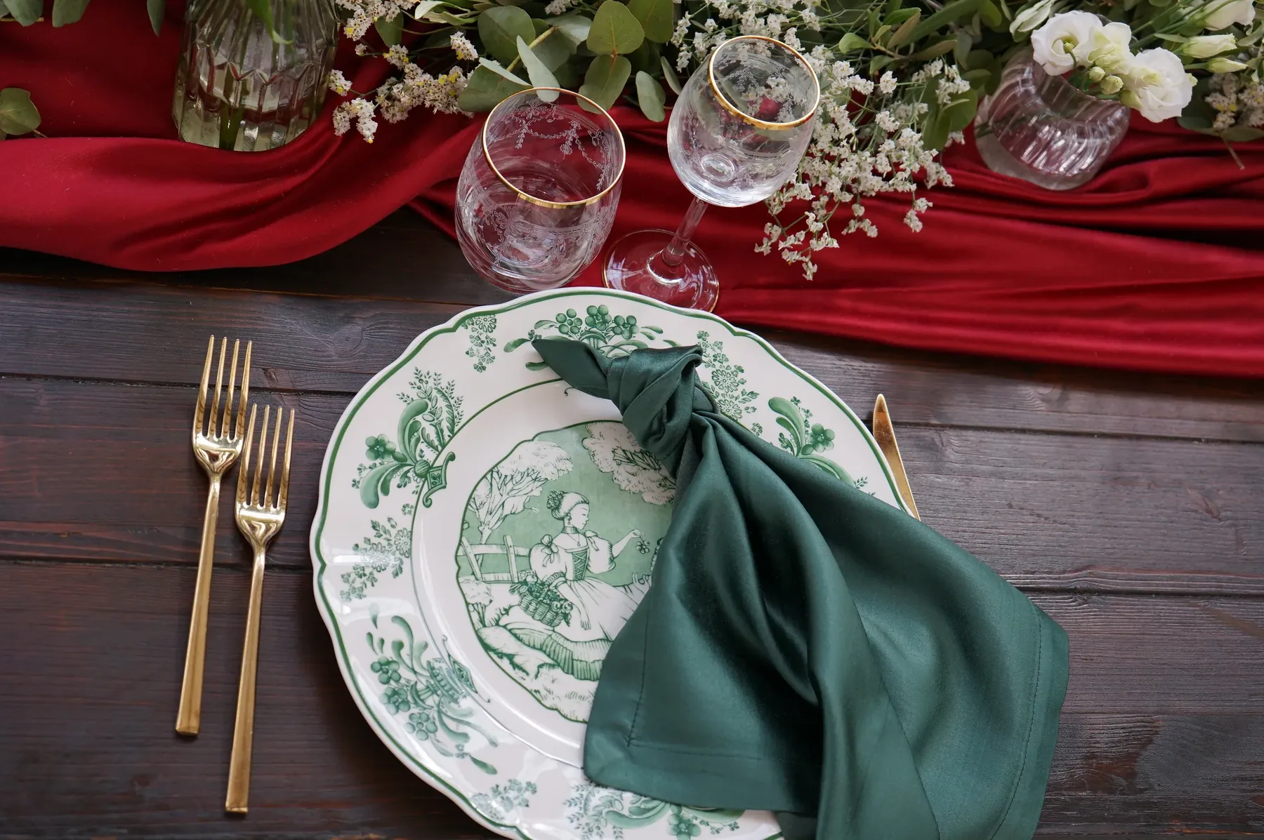 Tovagliolo verde annodato sul piatto a decoro verde, con il runner rosso e i calici bordati d'oro