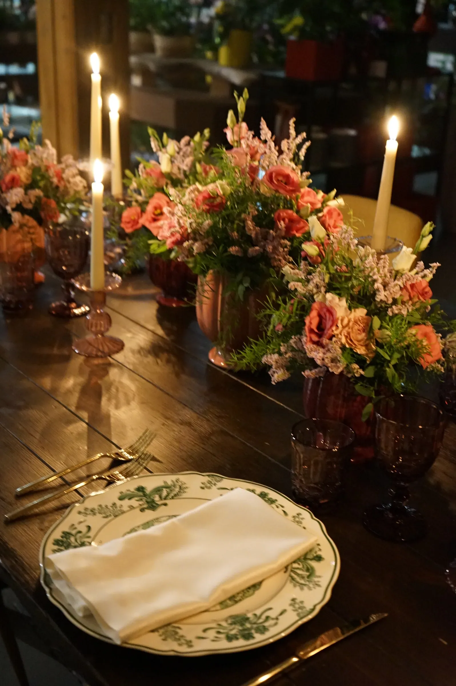 Rose e fiori arancio, candele accese e il piatto a decoro verde con il tovagliolo, di sera