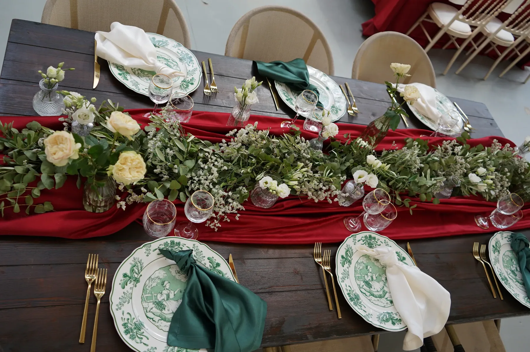 Runner rosso con fiori chiari ed edera lungo il tavolo di legno scuro, fra i piatti a decoro verde e i tovaglioli verdi