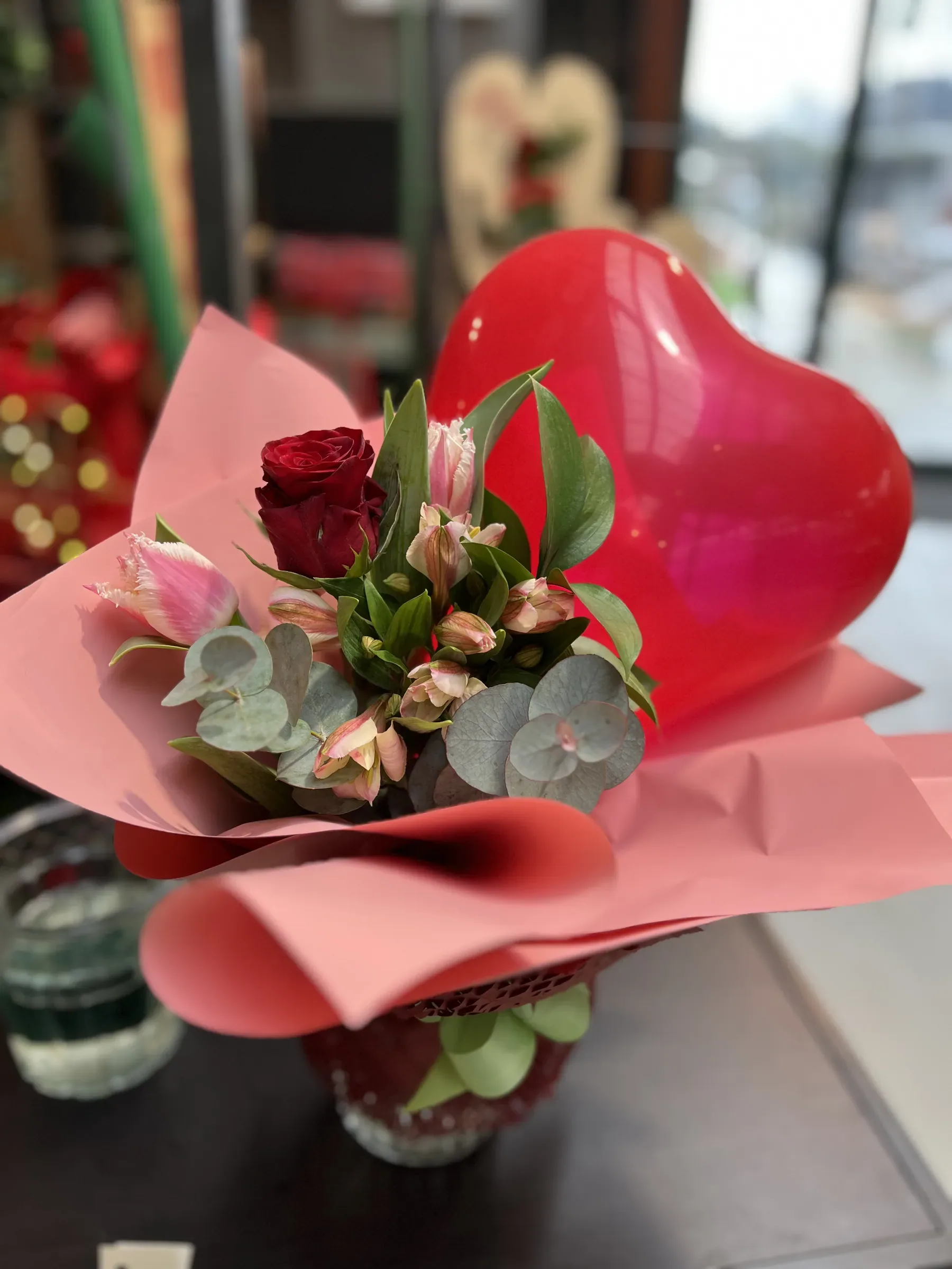 Una rosa rossa, alstroemerie rosa ed eucalipto in un vasetto incartato di rosa, con un palloncino rosso a cuore
