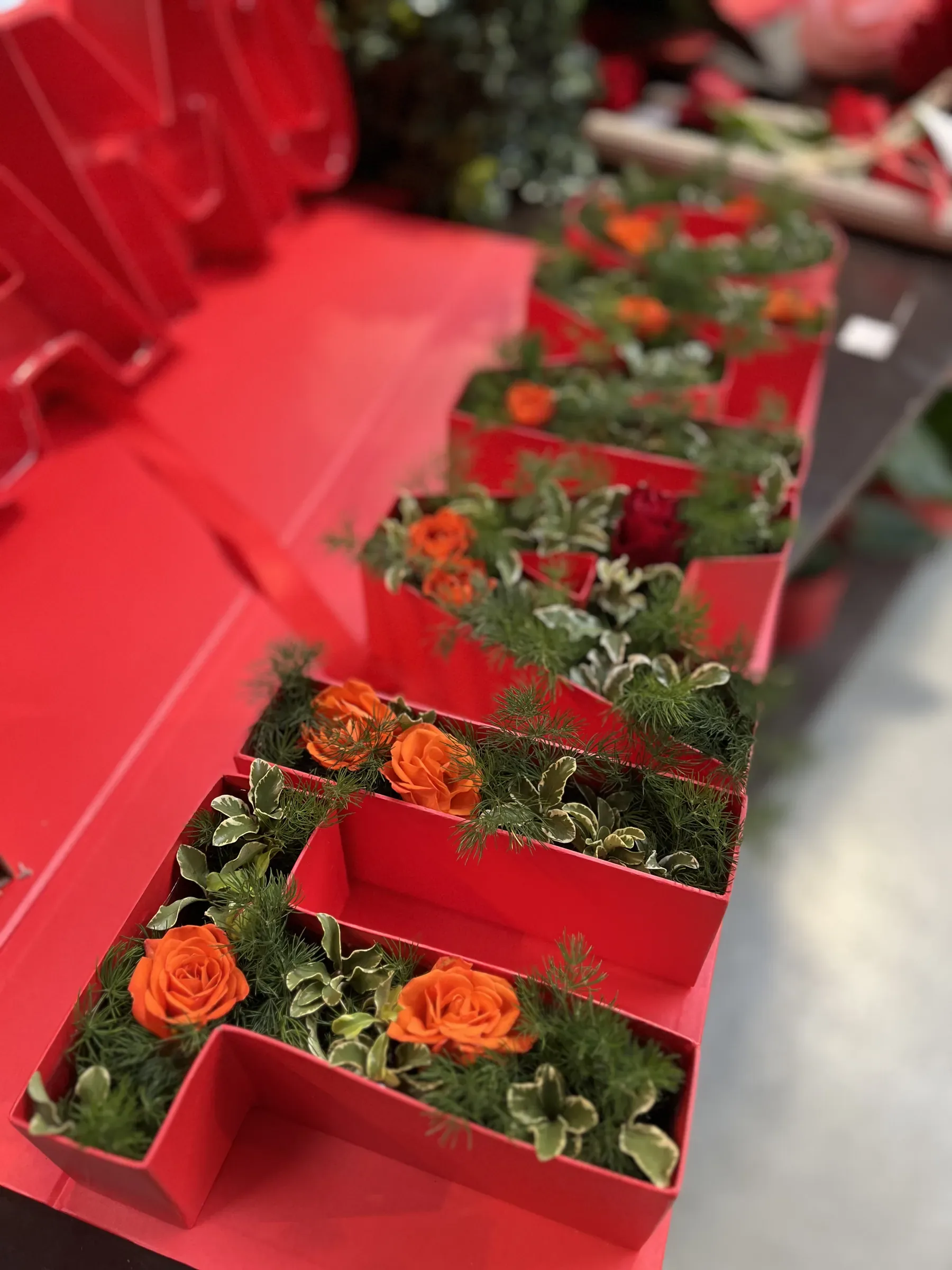 Scatole rosse a forma di lettera riempite di rose arancio e di verde, allineate sul banco