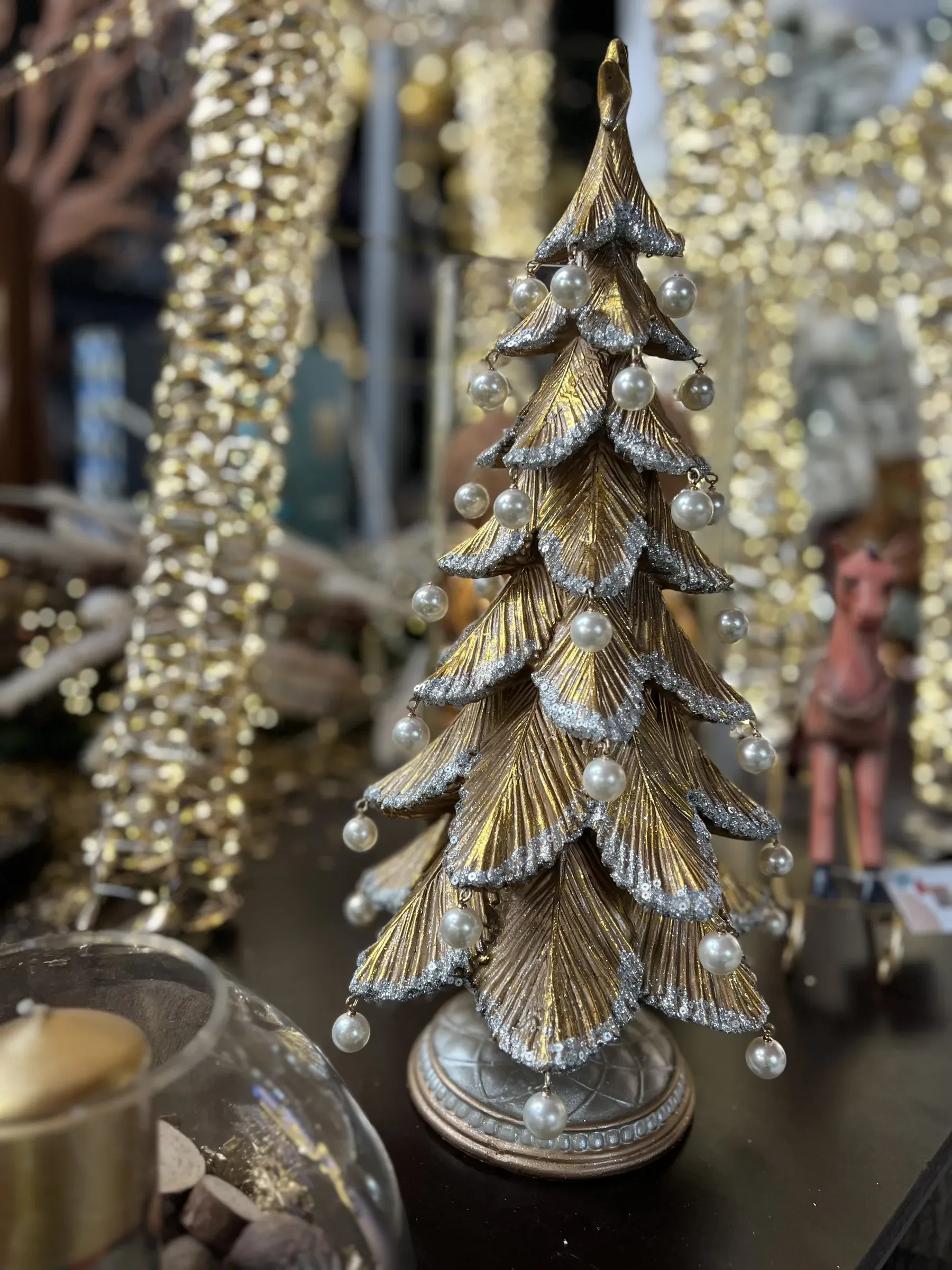 Alberello decorativo dorato con i bordi argentati e le perle appese, fra luci e decorazioni oro