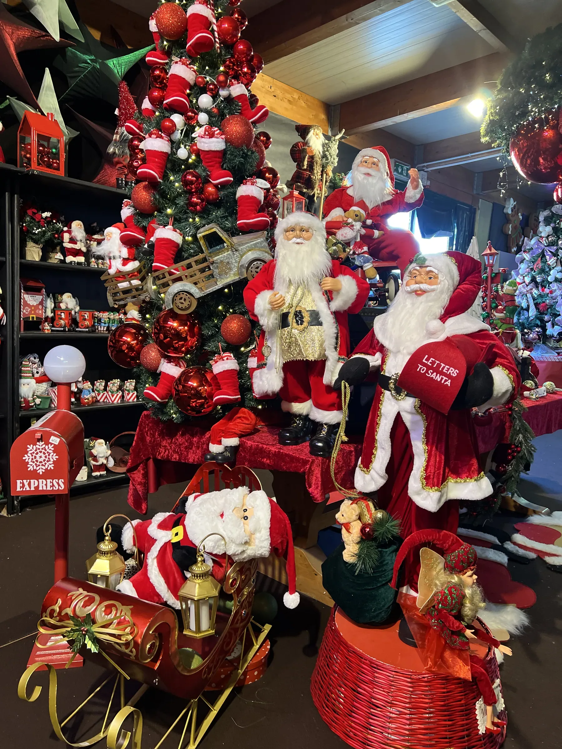 Pupazzi di Babbo Natale accanto a un albero addobbato di rosso, con una slitta, una cassetta delle lettere e scaffali di decorazioni