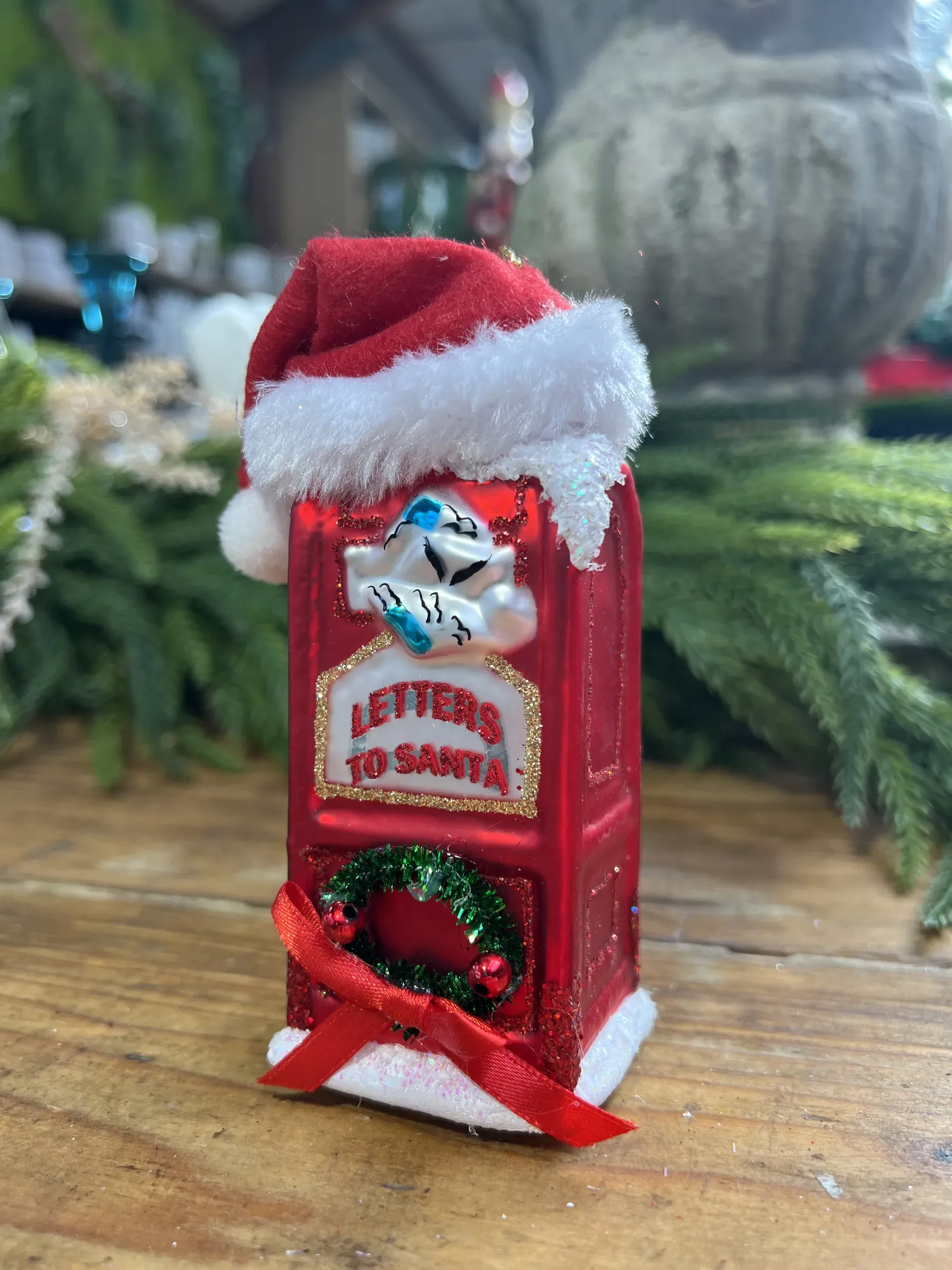 Cassetta rossa per le lettere a Babbo Natale con il cappello di pelo e una ghirlanda, su un tavolo di legno