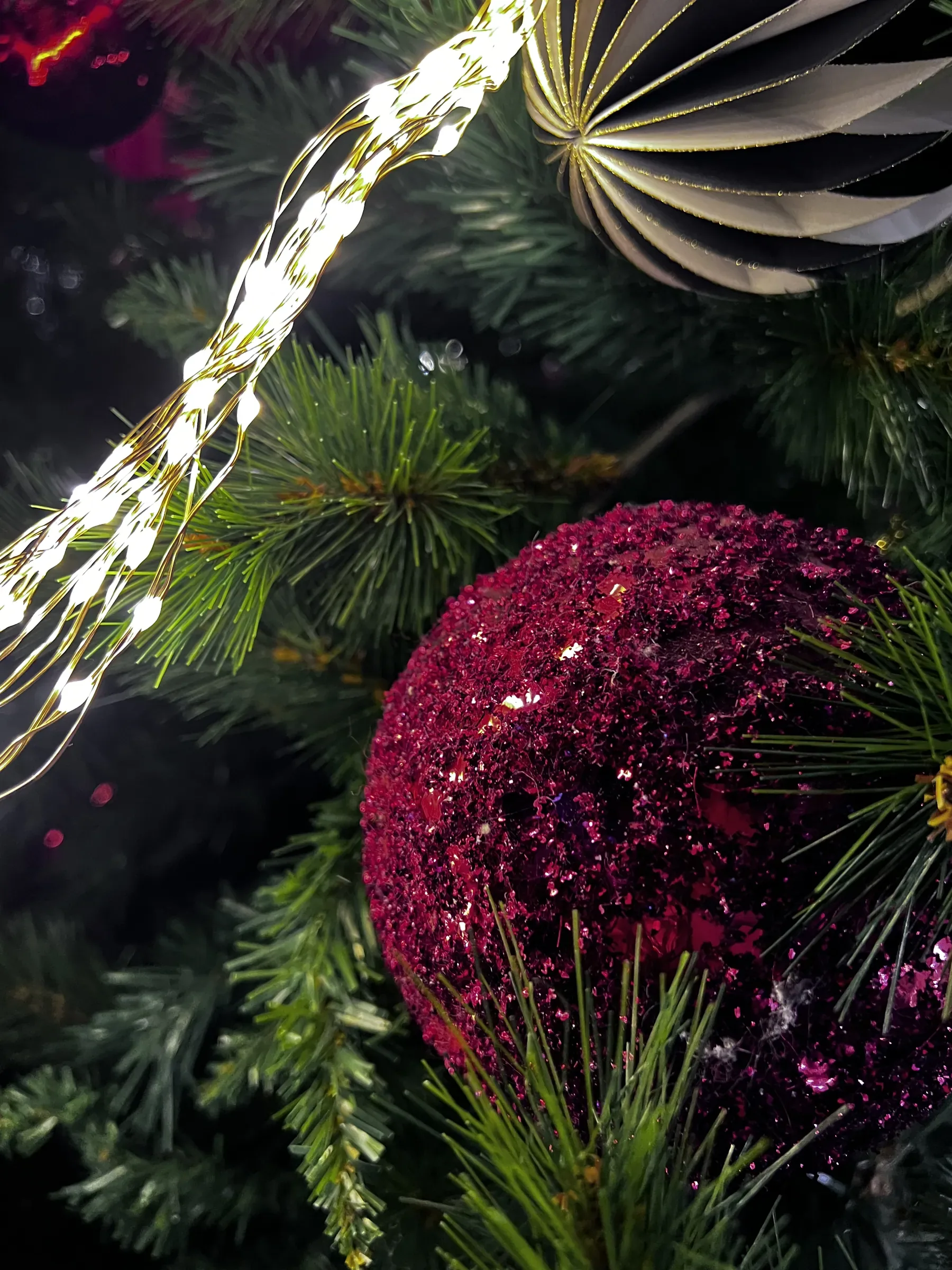 Pallina fucsia coperta di glitter fra i rami di un abete, con un filo di lucine