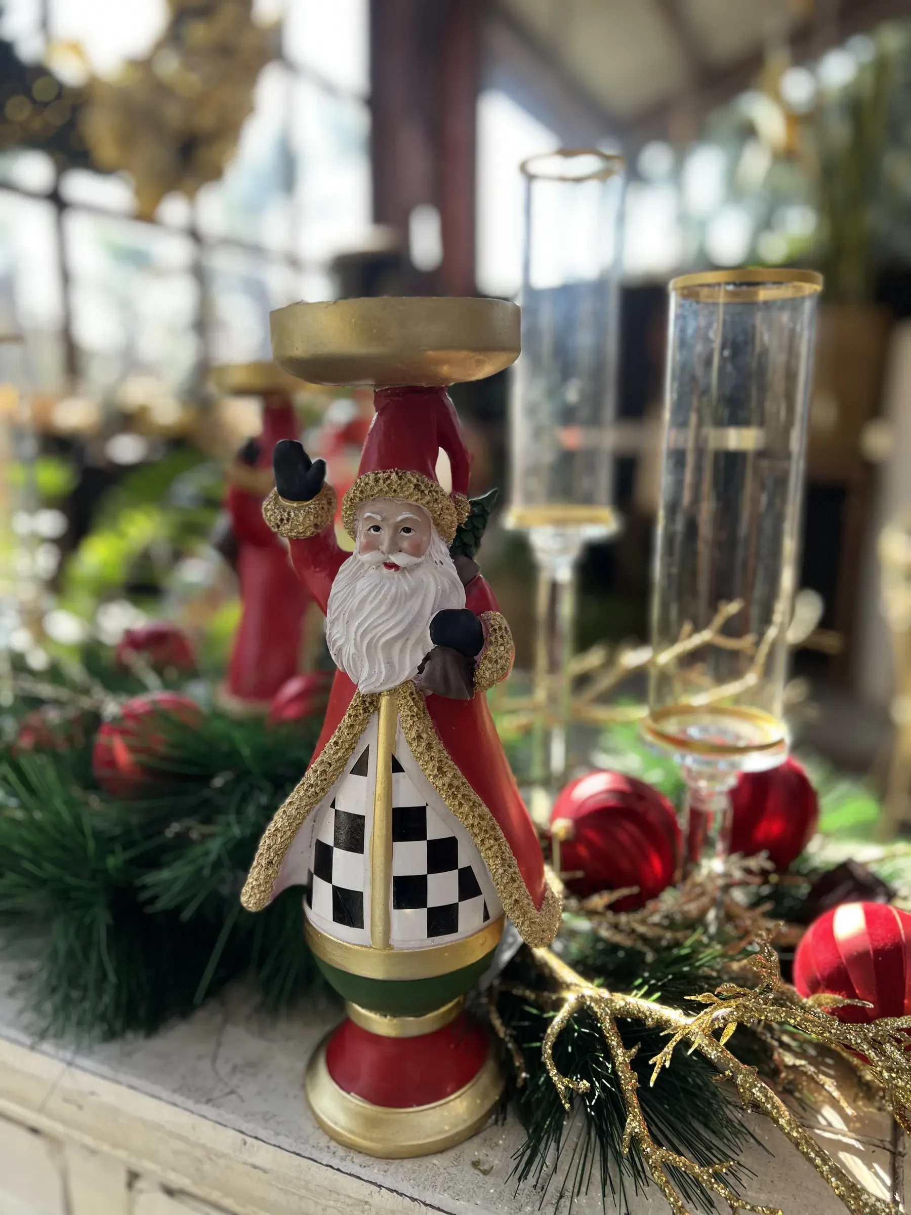 Portacandela a forma di Babbo Natale con il mantello a scacchi, fra rami di pino, palline rosse e flûte dorate