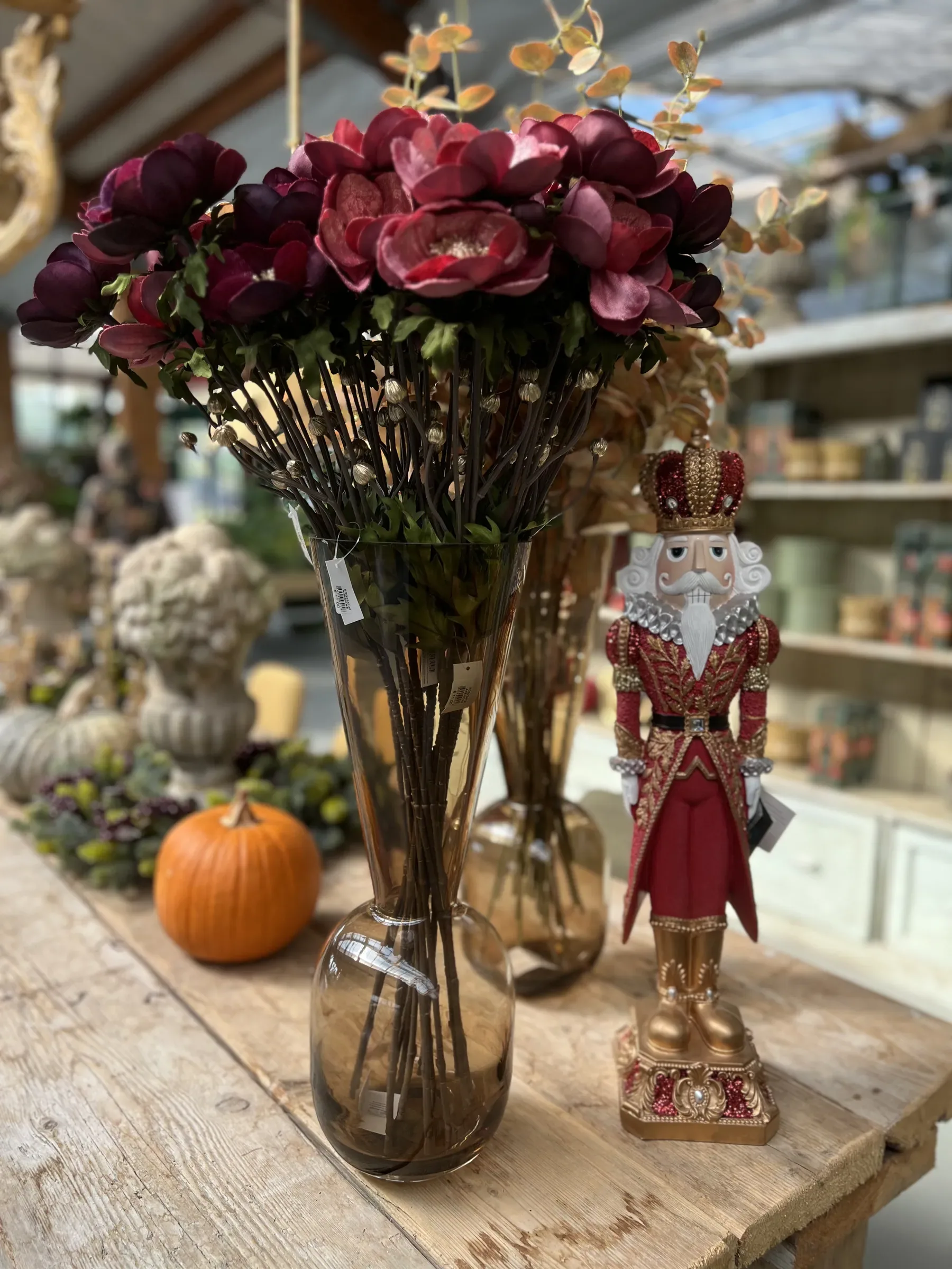 Fiori rosso scuro in un vaso di vetro fumé, uno schiaccianoci rosso e oro e una piccola zucca su un tavolo di legno chiaro