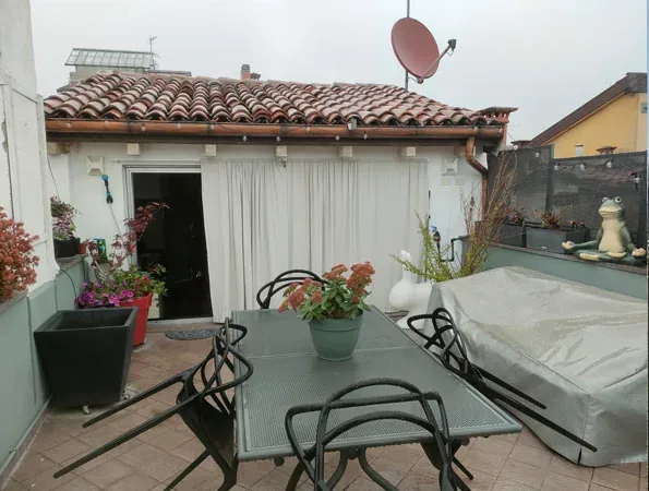 Prima: tavolo coperto da un telo, vasi di gerani e una tenda bianca davanti alla porta