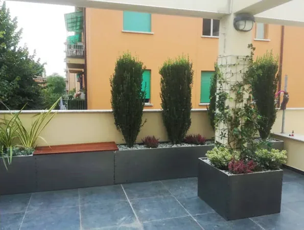 Dopo: fioriere scure con cipressi, una seduta in legno e un rampicante sul grigliato