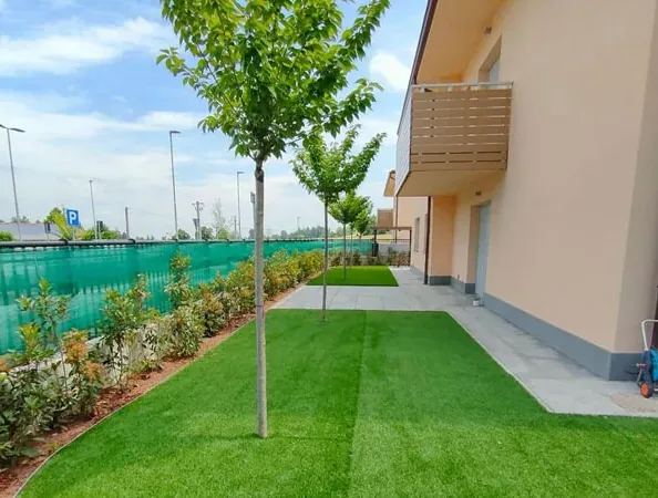Dopo: prato sintetico con un alberello al centro e una siepe giovane lungo la recinzione, accanto alla casa
