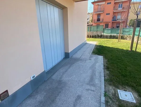 Prima: vialetto in cemento lungo il garage, con il prato ai lati e un pozzetto a terra