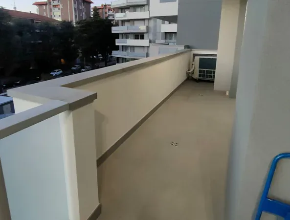 Prima: terrazzo lungo e vuoto, con il pavimento chiaro e il parapetto in muratura