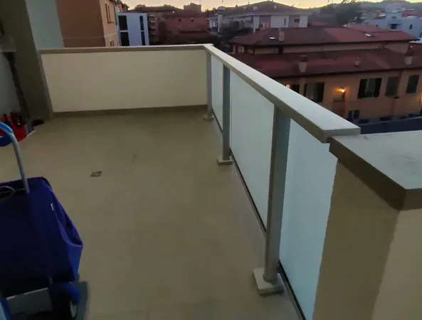 Prima: terrazzo vuoto con il parapetto in vetro, al tramonto, con un carrello delle pulizie in primo piano