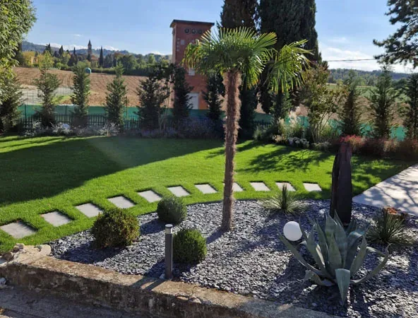 Dopo: prato con camminamento di lastre, palma e aiuole di ardesia, con i cipressi e la torretta in mattoni sul fondo