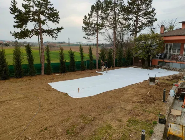 Prima: terreno spoglio con un telo bianco steso e la fila di cipressi lungo la recinzione