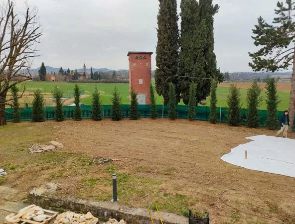 Prima: terreno spoglio con il telo bianco, i cipressi e la torretta in mattoni sul fondo