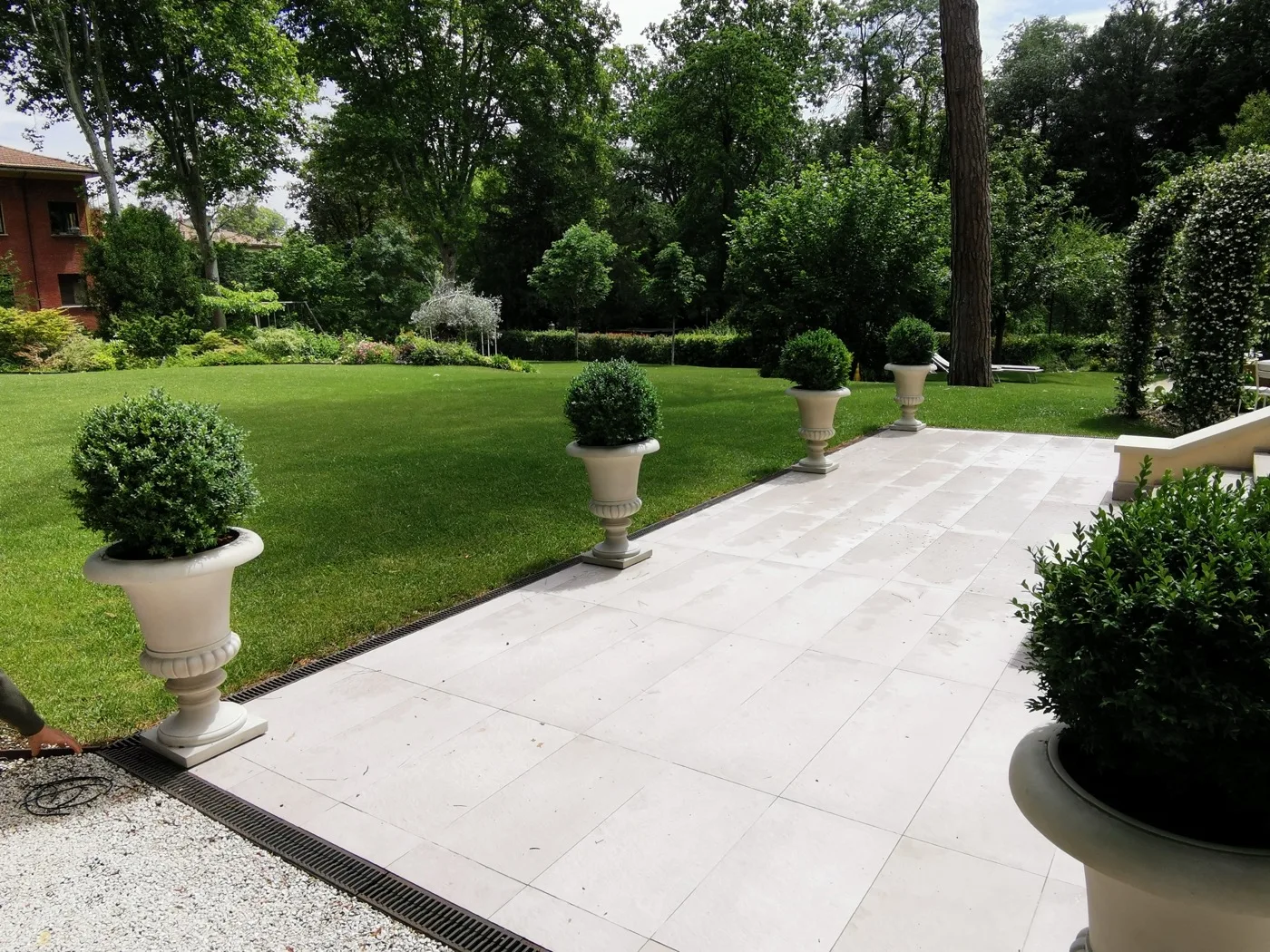 Camminamento in pietra chiara tra vasi di bosso e prato, in un giardino progettato da Sinflora