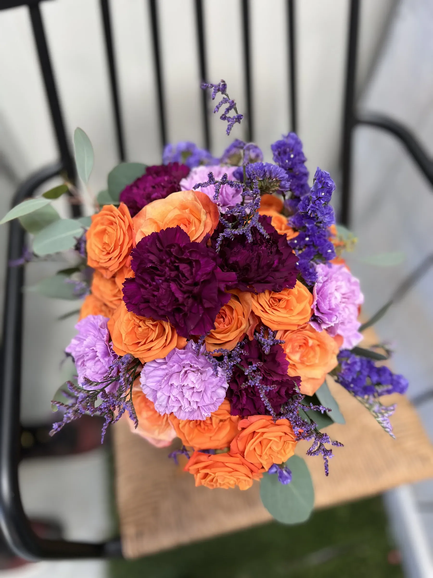 Mazzo rotondo di rose arancio, garofani viola e lilla e limonium, visto dall'alto
