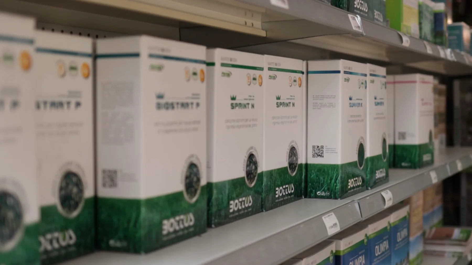 Scatole bianche e verdi di prodotti per il prato allineate sullo scaffale, viste di scorcio
